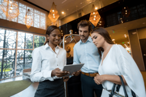 three employees smiling and gathering to look over one tablet in a hotel lobby