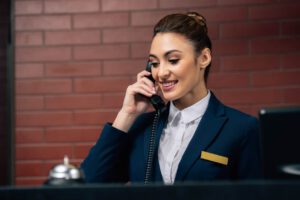 woman in a suit smiling and answering the phone behind a hotel front desk