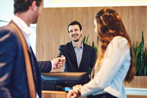 a male hotel employee handing a man a hotel key card from behind the desk