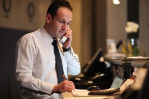 man in a white dress shirt and black tie on the phone behind a hotel desk