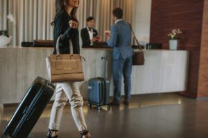 a woman holding a purse and a suitcase walking through a hotel lobby with the hotel concierge in the background