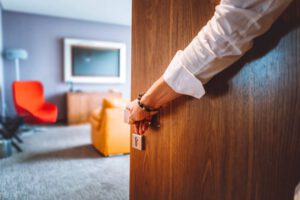 a close up of a hand opening a wooden hotel door with a hotel room out of focus in the back