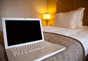 a laptop with a black screen sitting on a hotel room bed with a lamp on in the background