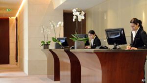 wooden hotel front desk with two female employees in suits working, orchids on the desks