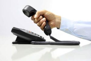 a hand holding a landline phone above the rest of the machine