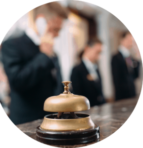 A concierge bell sitting on the counter of a desk at a hotel with employees in suits blurred out in the back